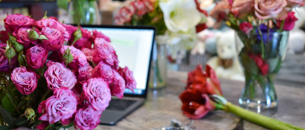 Computer on table with flowers around.